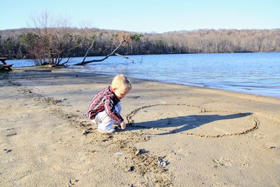 Side view of boy making heart shape at lakeshore