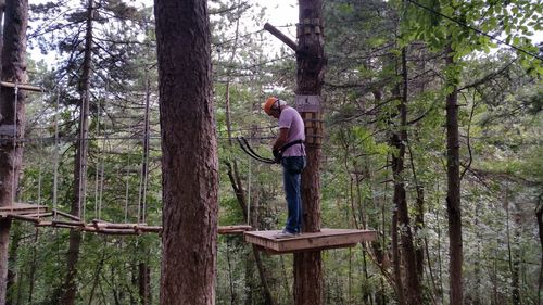 Man with zip line equipment standing on wooden platform at forest