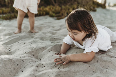 Close up of 2 year old playing in sand at beach while sister looks on