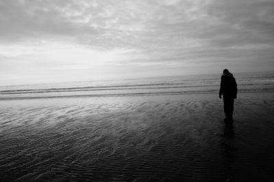 Rear view of man standing on beach against sky