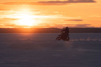 Man riding motorcycle on beach against sky during sunset