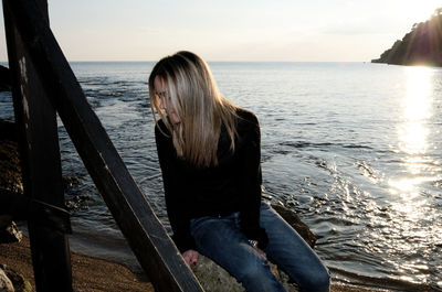 Woman sitting on railing by sea against sky