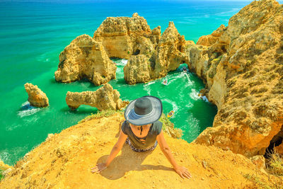 Rear view of woman sitting on cliff against sea