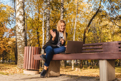 Woman using laptop while sitting on bench in park