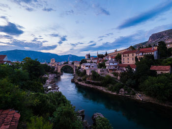 Arch bridge over river amidst buildings against sky