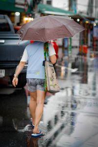 Rear view of woman with umbrella walking on street during rainy season