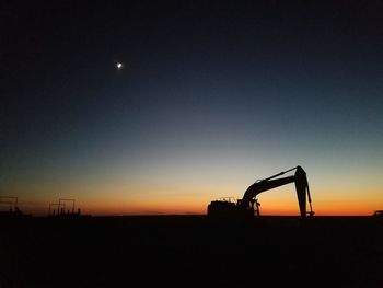 Silhouette bulldozer on field against sky during sunset