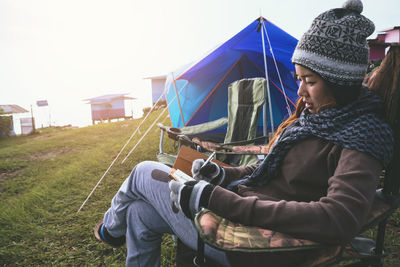 Side view of woman writing in diary while sitting on chair at campsite