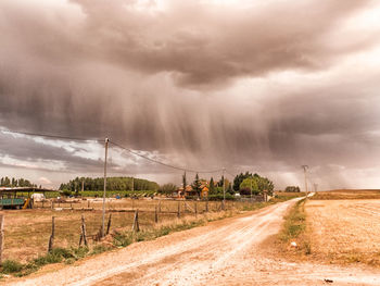 Road by trees against storm clouds