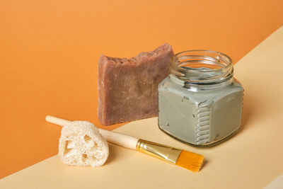 Cocoa soap, luffa, brush, cosmetic clay in a glass jar on a wooden stand, beige and brown background