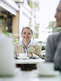 Smiling businesswoman sitting with coffee at sidewalk cafe