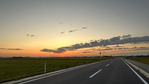 Road amidst field against sky during sunset