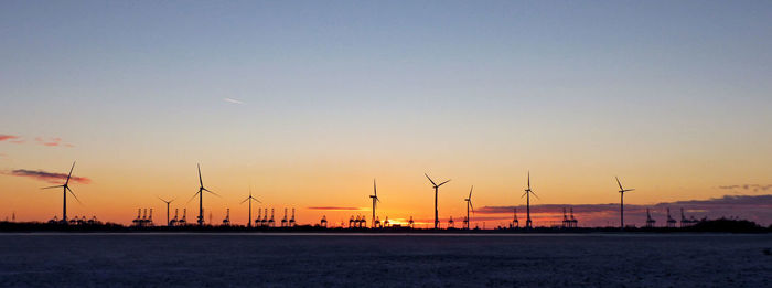 Panoramic view of silhouette windmills and river against orange sky during sunset