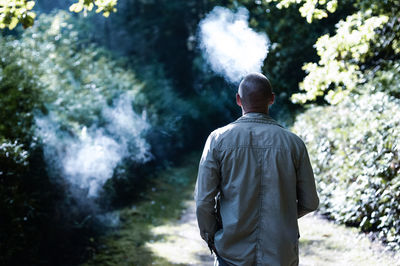 Rear view of man smoking while standing forest