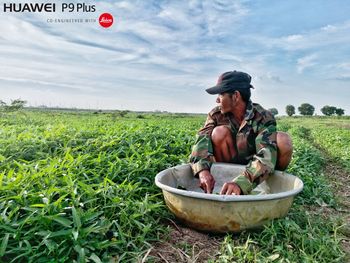 Man sitting on field against sky