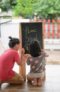 Rear view of sibling writing on the chalkboard 