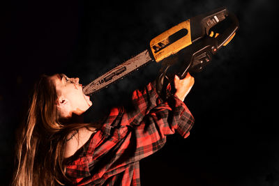 Young woman putting chainsaw in mouth at night