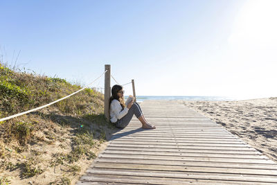 Girl reading book leaning on pole at beach