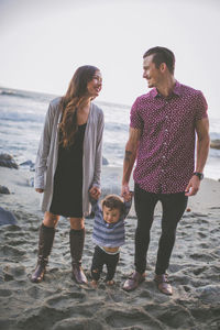 Parents holding son's hands while standing on sand at beach