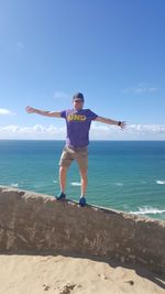 Man standing on railing at beach against blue sky