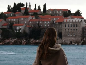 Rear view of woman by river against buildings