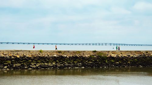 Tilt-shift image of people on pier at tagus river against sky