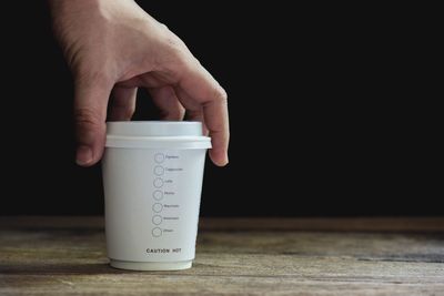 Close-up of hand holding coffee cup against black background