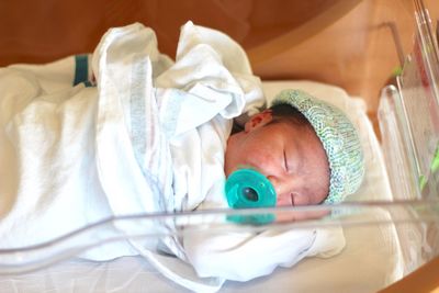 Cute baby girl sucking pacifier in crib