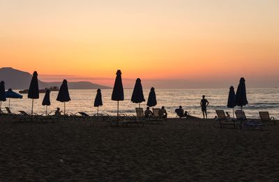 Silhouette people on beach against sky during sunset