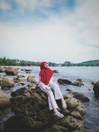 Woman sitting on rock at lakeshore against sky