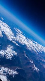 Aerial view of snowcapped mountains and sea against blue sky