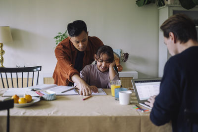 Gay man assisting happy daughter while studying at home