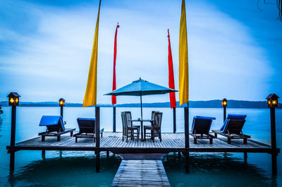 Chairs on swimming pool at beach against blue sky