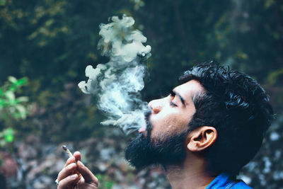 Profile view of young man smoking cigarette outdoors