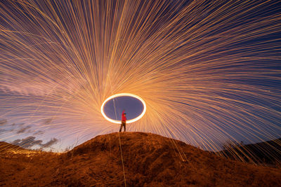 Low angle view of man spinning wire wool while standing on mountain against sky