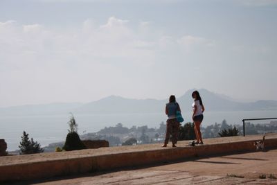 Rear view of people standing by lake against sky