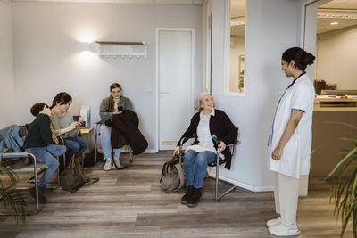 Female healthcare worker communicating with patients sitting in waiting room at healthcare center