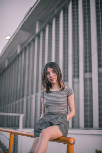 Portrait of smiling young woman sitting against built structure