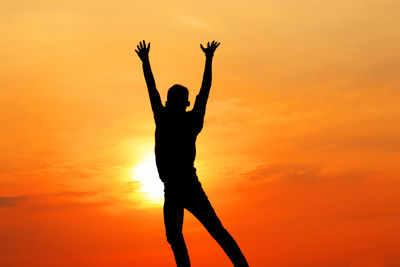 Silhouette woman with arms raised standing against orange sky