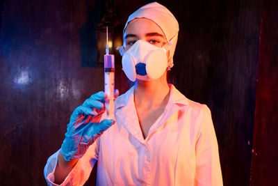 A woman in a white lab coat holding syringe. she is wearing mask and gloves