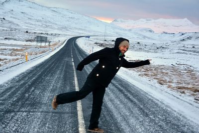 Full length portrait of smiling man gesturing by field on road during winter