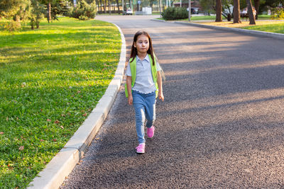 Young girl walking on park pathway with backpack in sunny weather