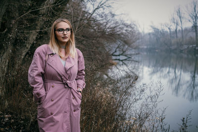 Portrait of beautiful woman standing by lake against sky during winter