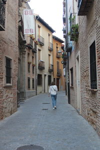 Rear view of woman walking on footpath amidst buildings