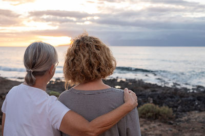 Rear view of woman looking at sea against sky during sunset