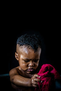 Shirtless baby boy holding napkin against black background