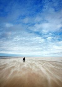 Rear view of man walking at beach against sky during winter