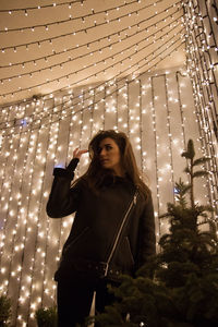 Full length of beautiful woman standing against illuminated wall