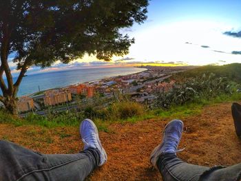 Low section of man relaxing on landscape against sky