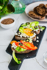 Appetizing sandwiches on rye bread with feta cheese, olives and vegetables on a slate board. 